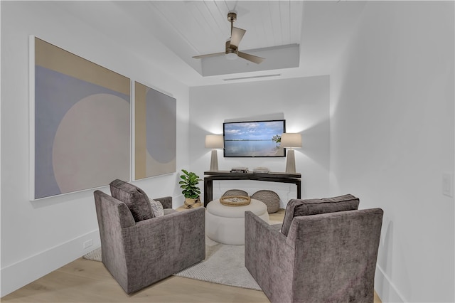 living room with light wood-type flooring, ceiling fan, and a tray ceiling