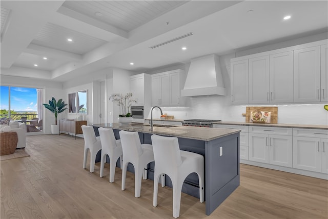 kitchen with white cabinets, a center island with sink, sink, and custom exhaust hood