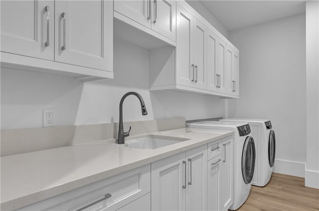 clothes washing area featuring sink, cabinets, washing machine and clothes dryer, and light hardwood / wood-style flooring