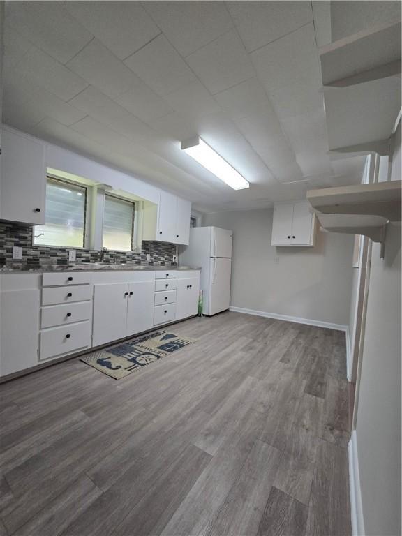 kitchen featuring decorative backsplash, freestanding refrigerator, white cabinets, wood finished floors, and baseboards