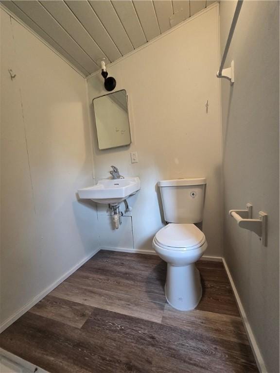 half bath with baseboards, toilet, wood finished floors, vaulted ceiling, and a sink