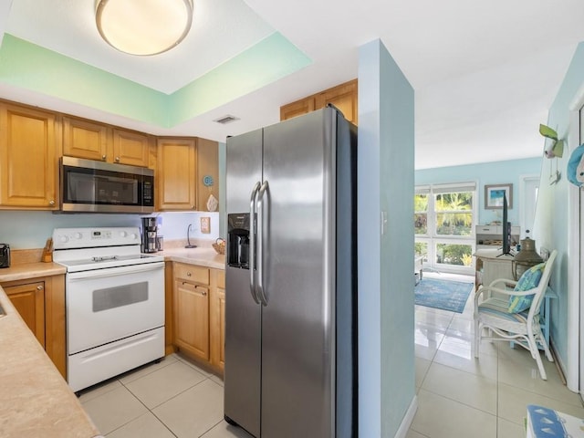 kitchen with light tile patterned floors, a raised ceiling, and stainless steel appliances