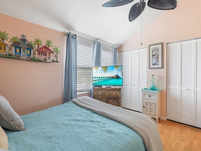 bedroom with ceiling fan, vaulted ceiling, light hardwood / wood-style floors, and two closets