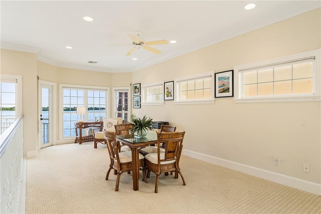 dining area featuring light carpet, ceiling fan, a healthy amount of sunlight, ornamental molding, and a water view