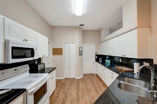 kitchen featuring sink, white appliances, light hardwood / wood-style flooring, white cabinets, and dark stone counters