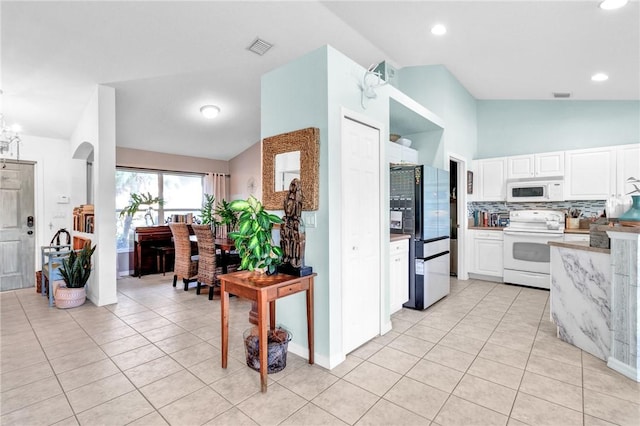 kitchen with lofted ceiling, white appliances, white cabinets, tasteful backsplash, and light tile patterned flooring