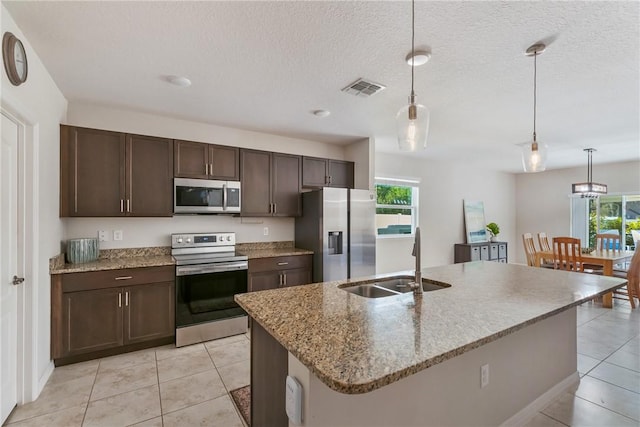 kitchen with hanging light fixtures, appliances with stainless steel finishes, sink, and a center island with sink