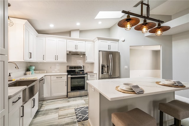 kitchen with light stone counters, appliances with stainless steel finishes, vaulted ceiling with skylight, and white cabinets