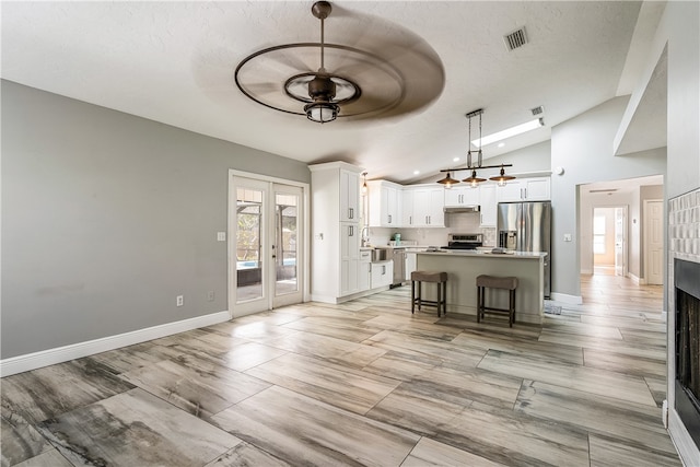 kitchen with a kitchen bar, white cabinetry, a center island, vaulted ceiling, and hanging light fixtures