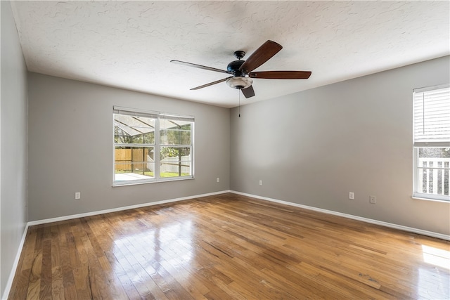 empty room featuring ceiling fan, hardwood / wood-style flooring, a textured ceiling, and a healthy amount of sunlight