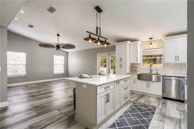 kitchen featuring sink, vaulted ceiling, stainless steel dishwasher, a kitchen island, and white cabinets