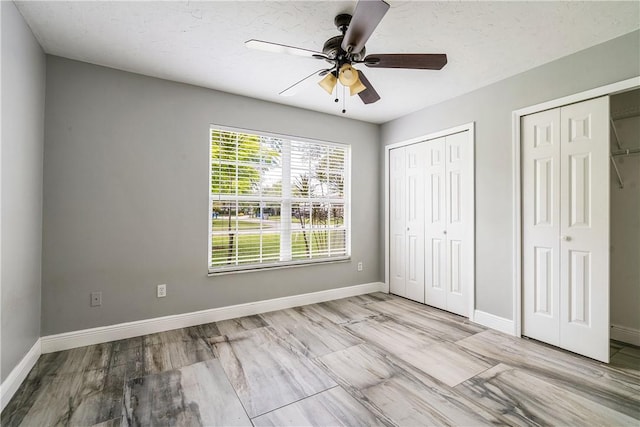 unfurnished bedroom featuring multiple closets, baseboards, and ceiling fan