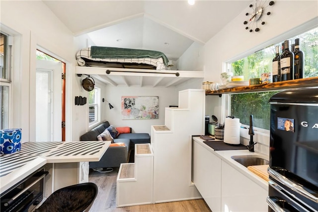 kitchen featuring white cabinets, vaulted ceiling with beams, light hardwood / wood-style floors, and plenty of natural light