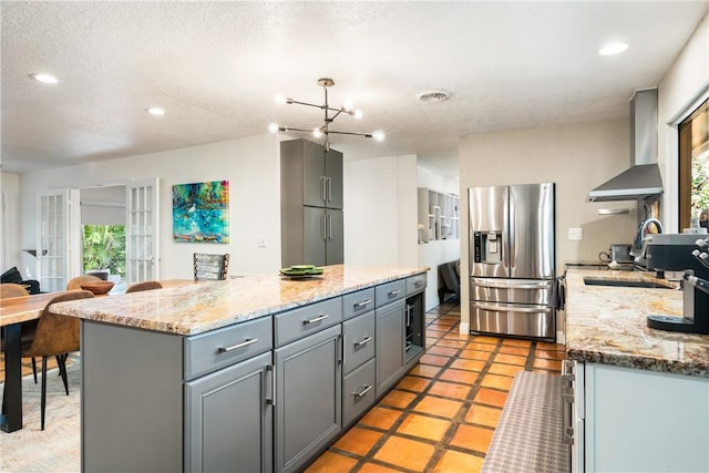 kitchen with stainless steel fridge, a center island, wall chimney exhaust hood, and gray cabinetry