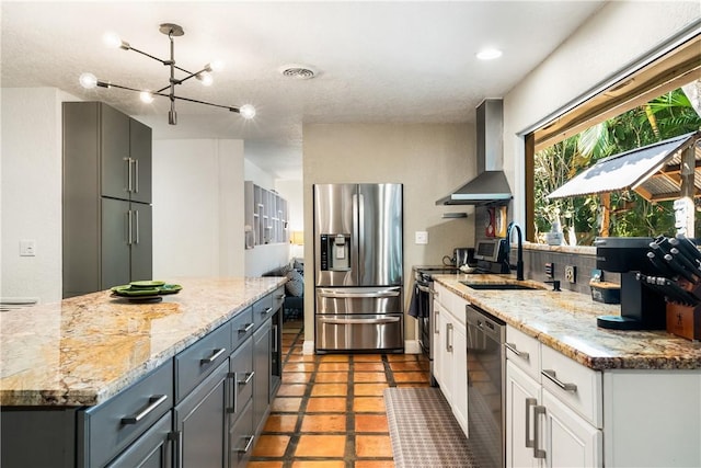 kitchen with stainless steel appliances, sink, wall chimney range hood, white cabinets, and a chandelier