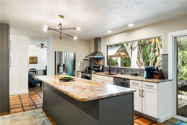 kitchen with stainless steel appliances, sink, wall chimney range hood, white cabinets, and a center island