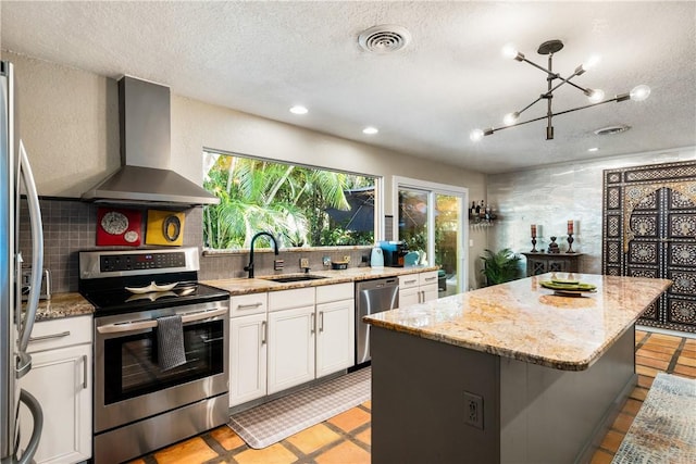 kitchen with wall chimney range hood, sink, decorative backsplash, appliances with stainless steel finishes, and a kitchen island