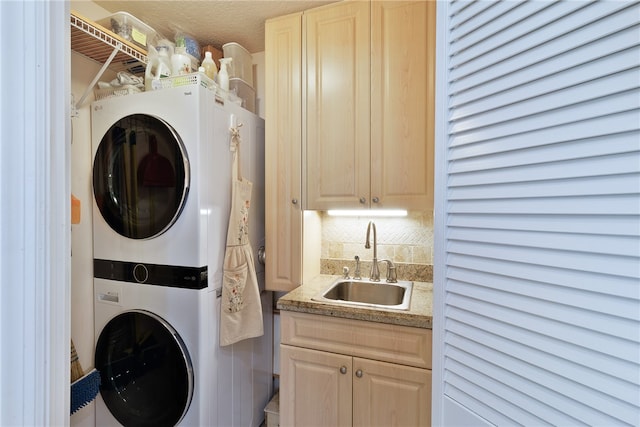 laundry area with cabinets, a textured ceiling, stacked washer / dryer, and sink