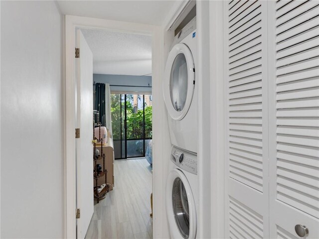 laundry room featuring a textured ceiling, light hardwood / wood-style floors, and stacked washer and clothes dryer