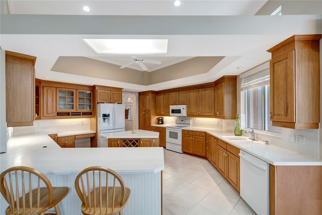 kitchen with a tray ceiling, a peninsula, a skylight, white appliances, and a sink