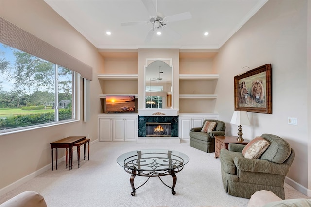 living room with built in shelves, baseboards, light carpet, a fireplace, and a ceiling fan