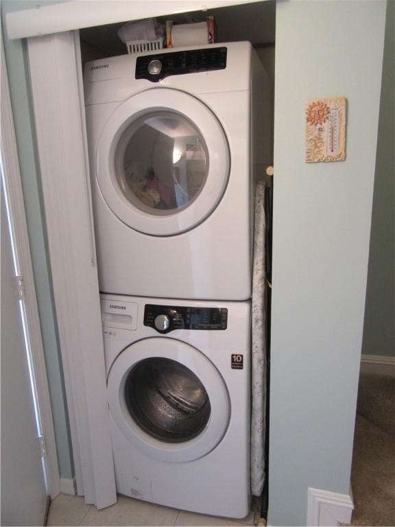 laundry area with stacked washer / dryer and light tile patterned flooring