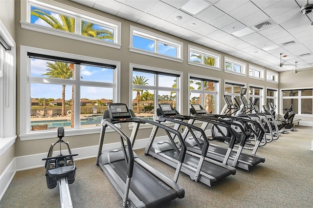 exercise room featuring baseboards, a high ceiling, visible vents, and a healthy amount of sunlight