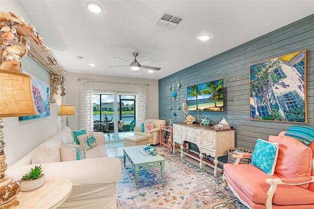 living room with wooden walls, visible vents, a ceiling fan, and recessed lighting