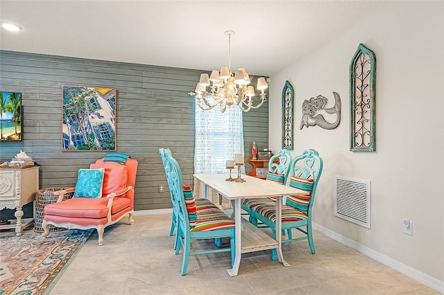 dining space with a chandelier, visible vents, wood walls, and baseboards