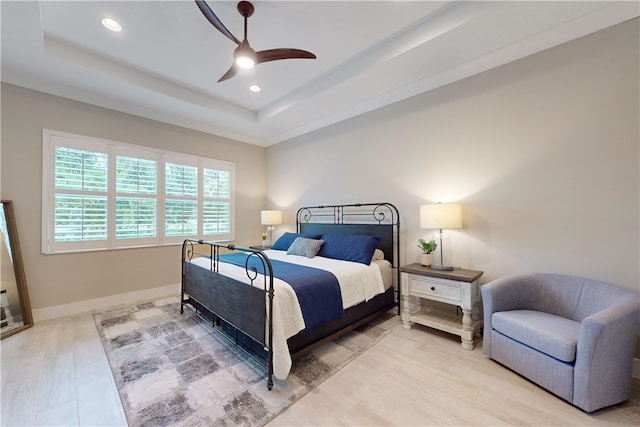 bedroom with light hardwood / wood-style flooring, ceiling fan, and a tray ceiling