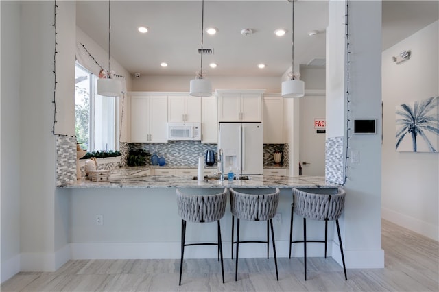 kitchen with white cabinets, light stone counters, white appliances, and decorative light fixtures