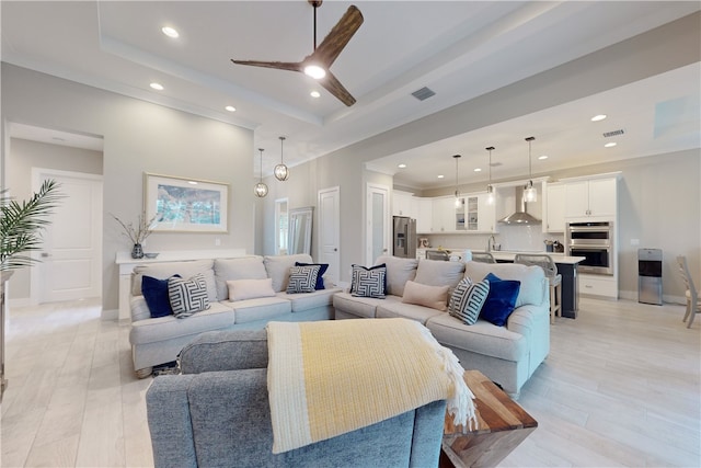 living room featuring light hardwood / wood-style floors, ceiling fan, and a tray ceiling