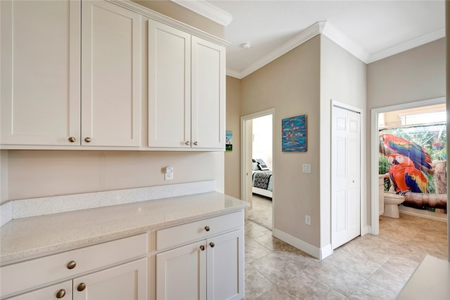 kitchen with white cabinetry, light stone counters, and ornamental molding