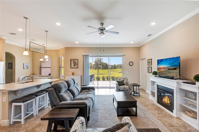 living room with ceiling fan with notable chandelier, sink, light tile patterned floors, and crown molding