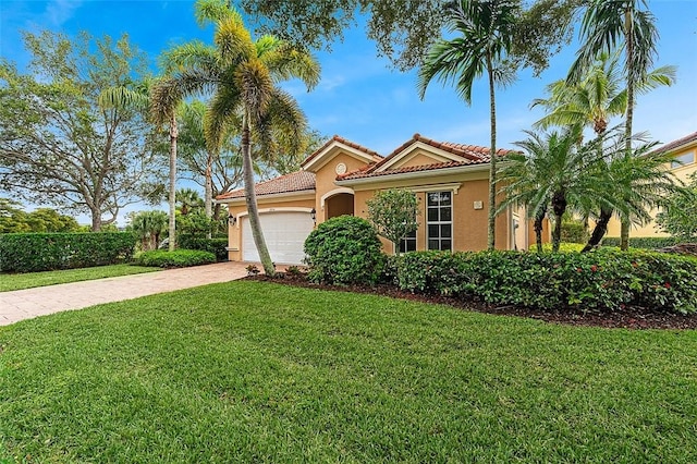 mediterranean / spanish-style house with stucco siding, driveway, a front yard, a garage, and a tiled roof