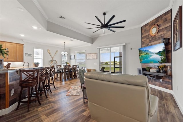 living room featuring dark wood-type flooring, ceiling fan with notable chandelier, and ornamental molding