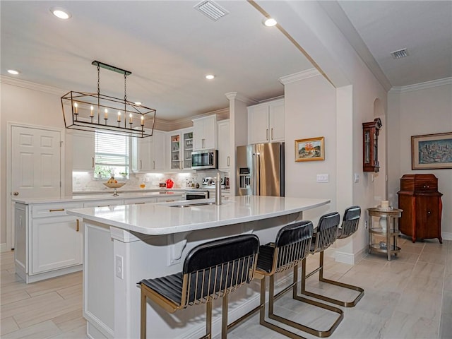 kitchen with a center island with sink, appliances with stainless steel finishes, sink, white cabinetry, and backsplash