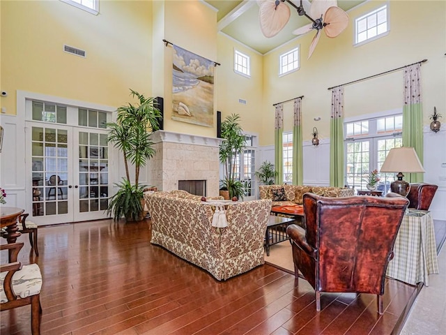 living room with a towering ceiling, french doors, ceiling fan, and a stone fireplace