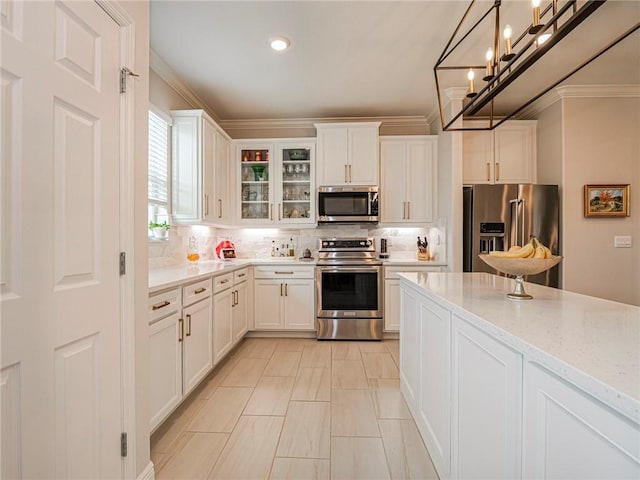 kitchen featuring appliances with stainless steel finishes, hanging light fixtures, white cabinetry, and light stone countertops