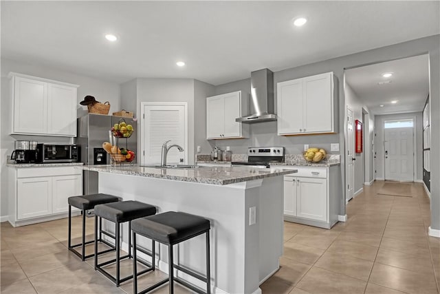 kitchen featuring stainless steel electric stove, white cabinets, wall chimney exhaust hood, and a kitchen island with sink