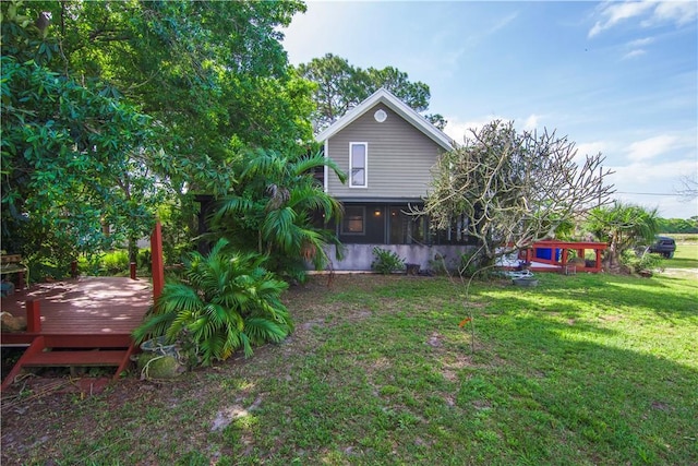 back of house featuring a sunroom, a lawn, and a wooden deck