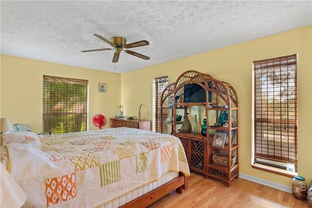 bedroom featuring light wood finished floors, a ceiling fan, baseboards, and a textured ceiling