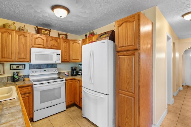 kitchen with arched walkways, light tile patterned floors, tile counters, a textured ceiling, and white appliances