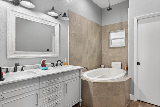 full bathroom featuring wood finished floors, a garden tub, a sink, and double vanity