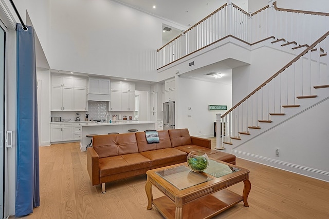 living room featuring a towering ceiling, light hardwood / wood-style flooring, and crown molding