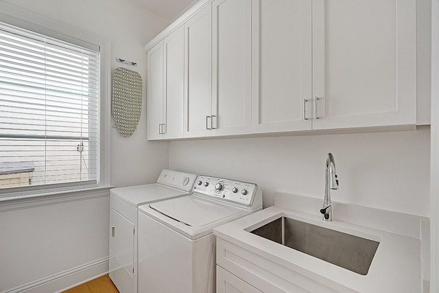 clothes washing area featuring cabinets, sink, washer and dryer, and light hardwood / wood-style floors