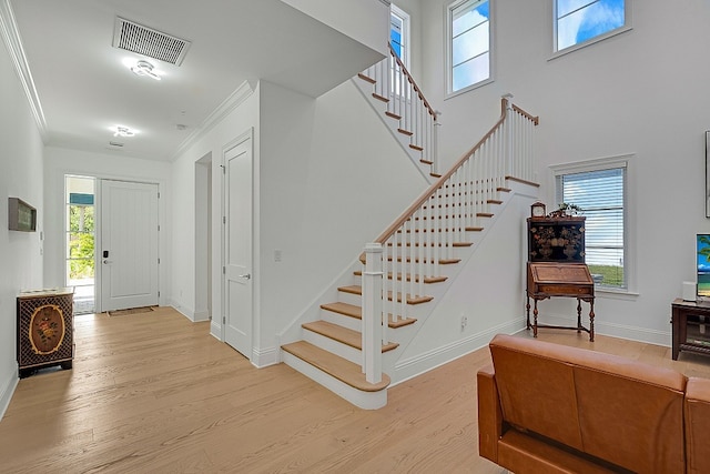 entrance foyer with ornamental molding, a wealth of natural light, and light hardwood / wood-style flooring