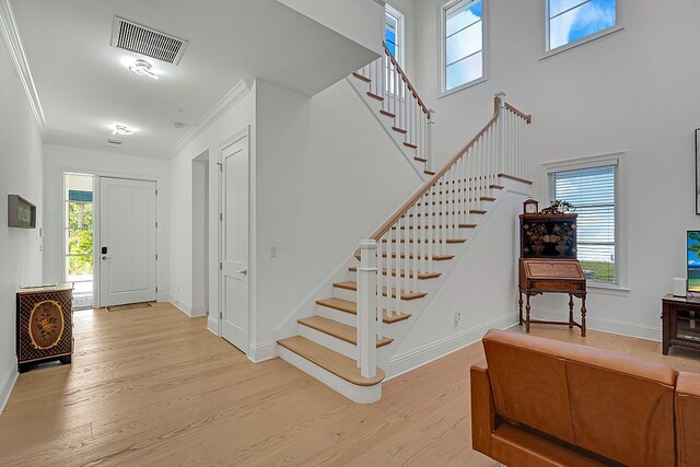 entrance foyer with ornamental molding, a wealth of natural light, and light hardwood / wood-style flooring