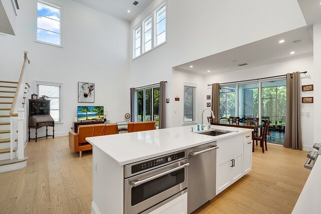 kitchen with a towering ceiling, appliances with stainless steel finishes, sink, white cabinets, and light hardwood / wood-style flooring