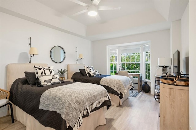 bedroom with light wood-type flooring, a tray ceiling, and ceiling fan